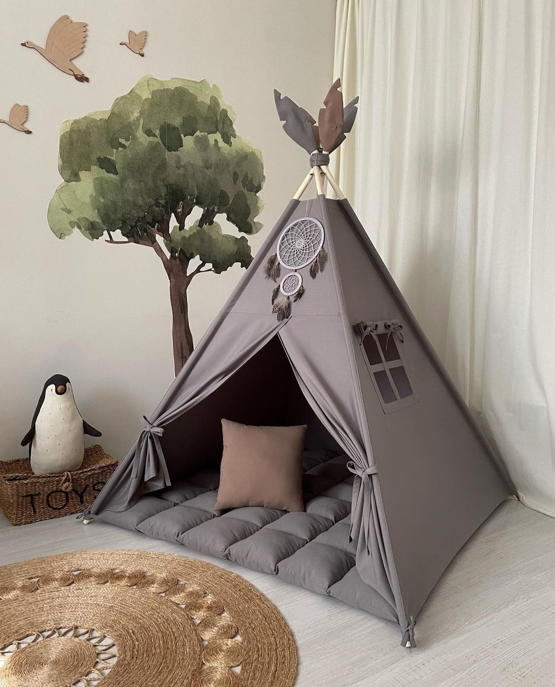 Dečiji šator postavljen u sobi. Šator je tamno sive boje i ukrašen hvatačem snova,,ispod vrha stoji jedan prozor, dok na vrhu ima dekorativne dodatke u obliku ptica. Unutrašnjost šatora sadrži mekani dušek i jastuk, što ga čini pogodnim za igru i odmor. U pozadini je zid sa slikom drveta i ptica, dok je pored šatora korpa za igračke i plišani pingvin. Na podu se nalazi okrugli tepih.
